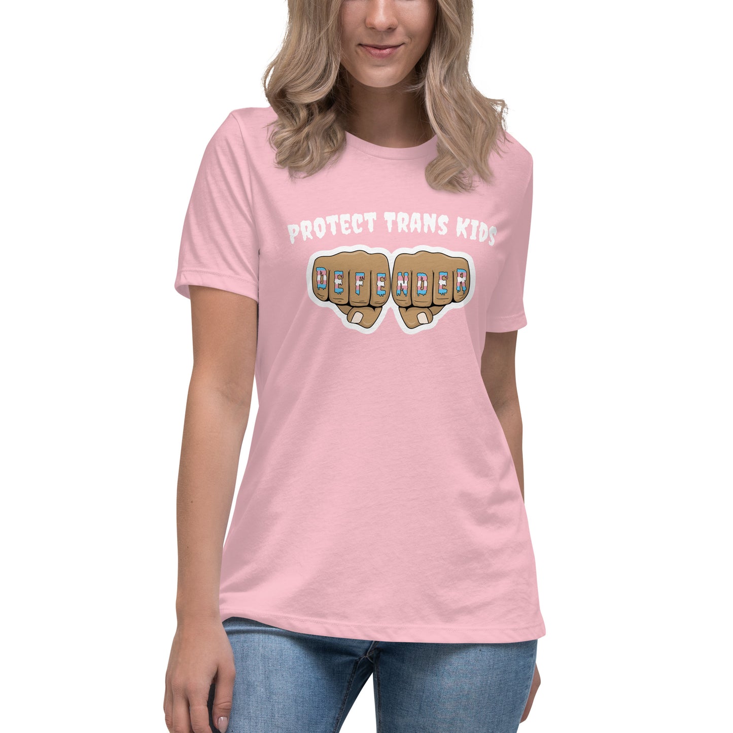 A standard, round neck, short sleeve t-shirt in light pink with the text "protect trans kids" in white lettering above an image of fists with "defender" written across the knuckles in blue,pink, and white. The shirt is on a white, straight sized model standing against a white background.