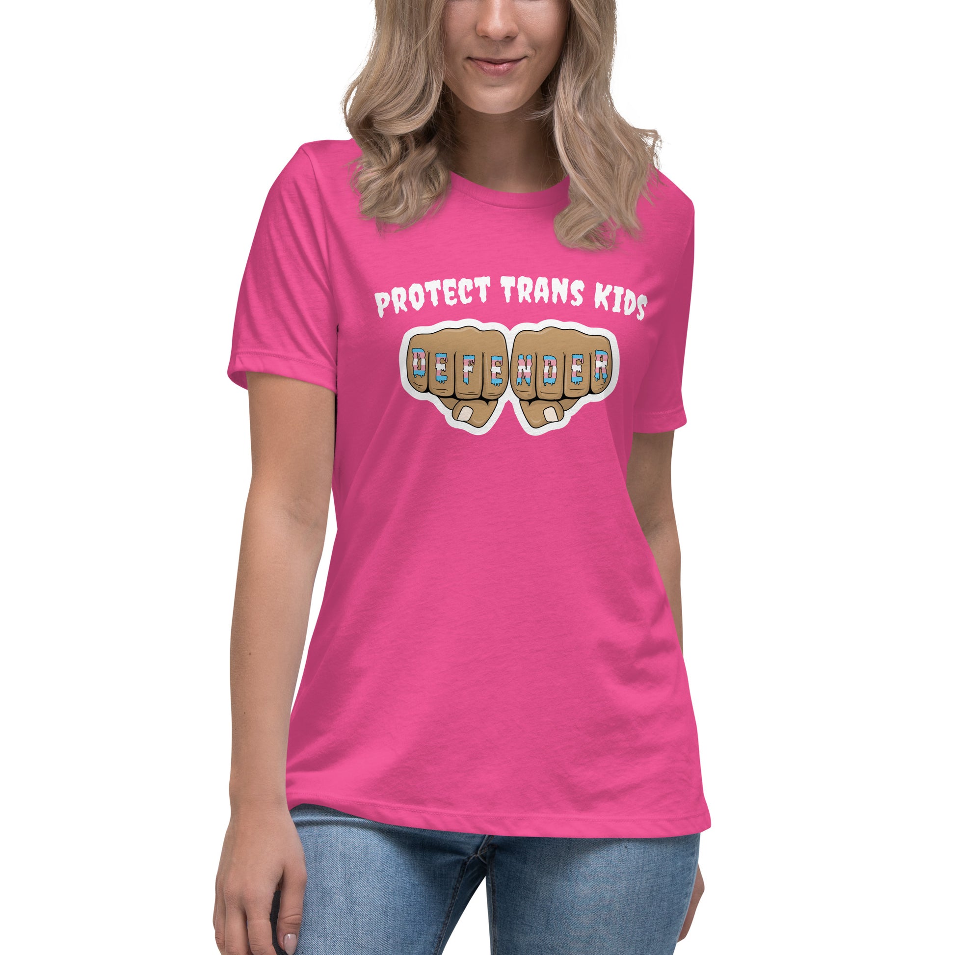 A standard, round neck, short sleeve t-shirt in pink with the text "protect trans kids" in white lettering above an image of fists with "defender" written across the knuckles in blue,pink, and white. The shirt is on a white, straight sized model standing against a white background.